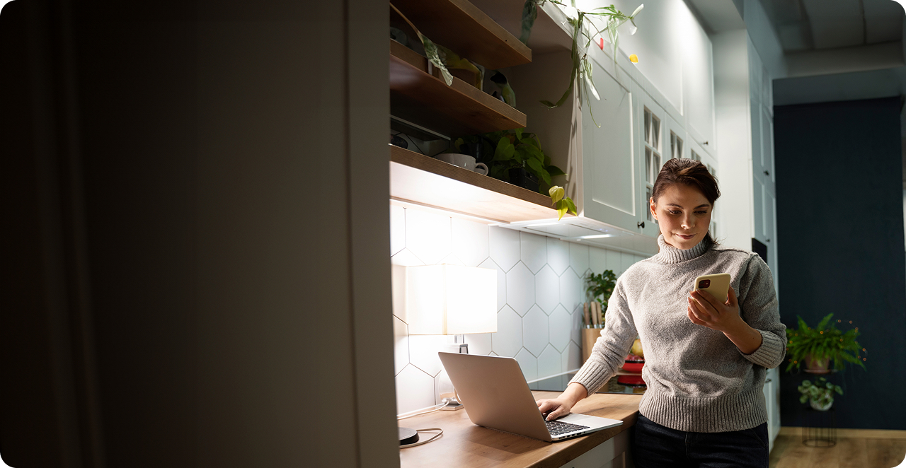 Woman in kitchen using laptop and phone